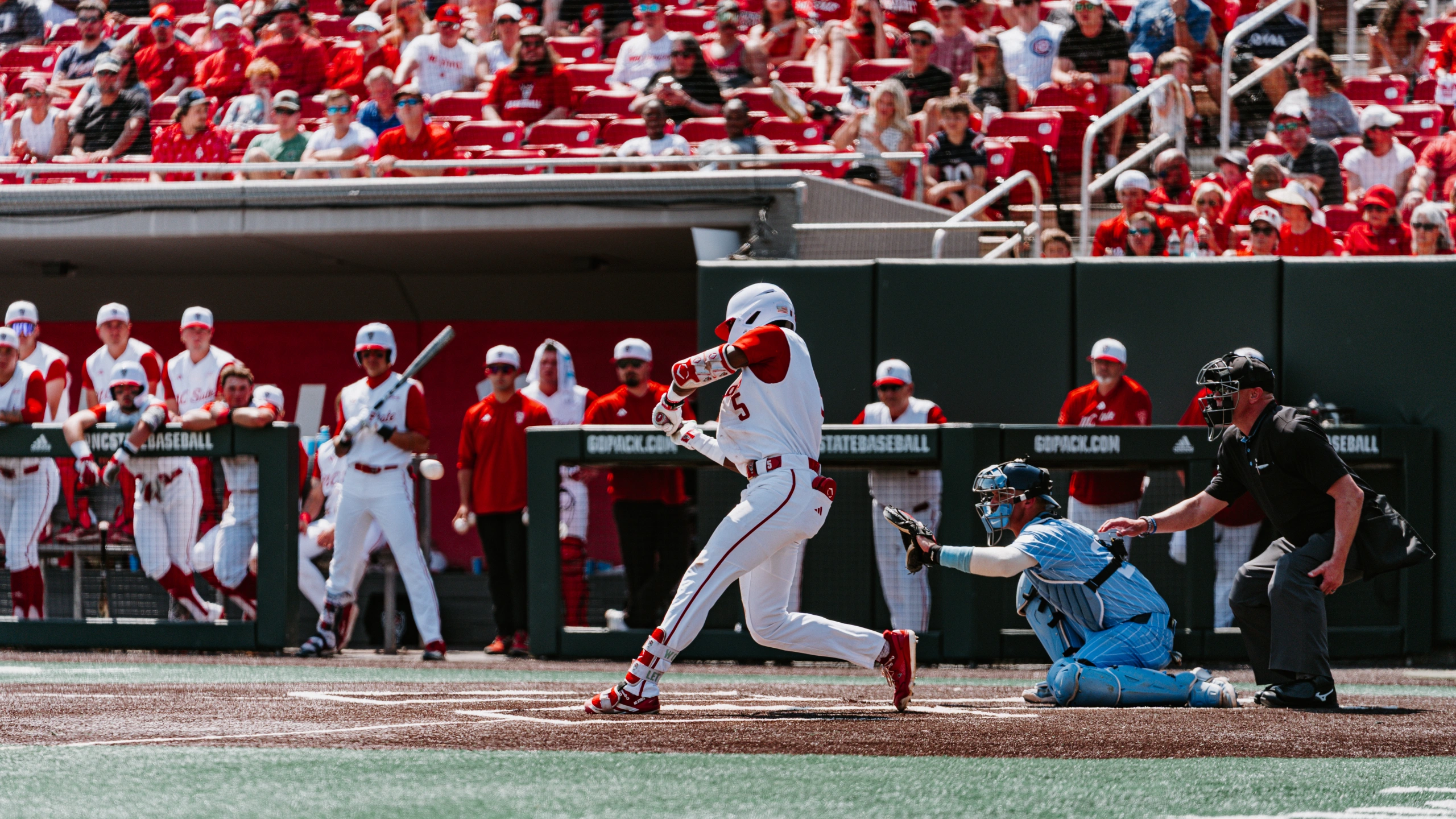 An NC State hitter at the moment of contact in front of a packed grandstand